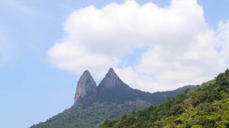 The twin peaks of Tioman island rising above the sea and green coastline