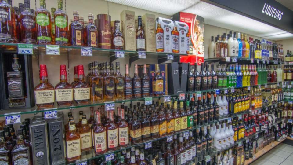 Long retail shelf stocked with rows of whisky and spirit bottles