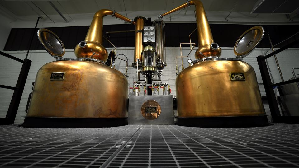 Two large copper pot stills facing the camera inside a whiskey distillery still house