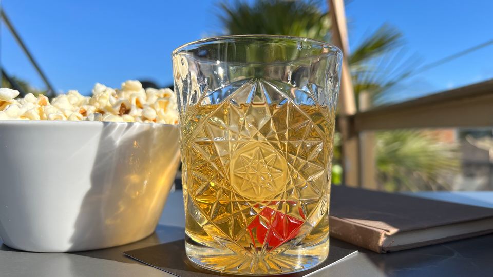 Smoky Old Fashioned cocktail in a cut-glass tumbler with a cherry, served outdoors with popcorn