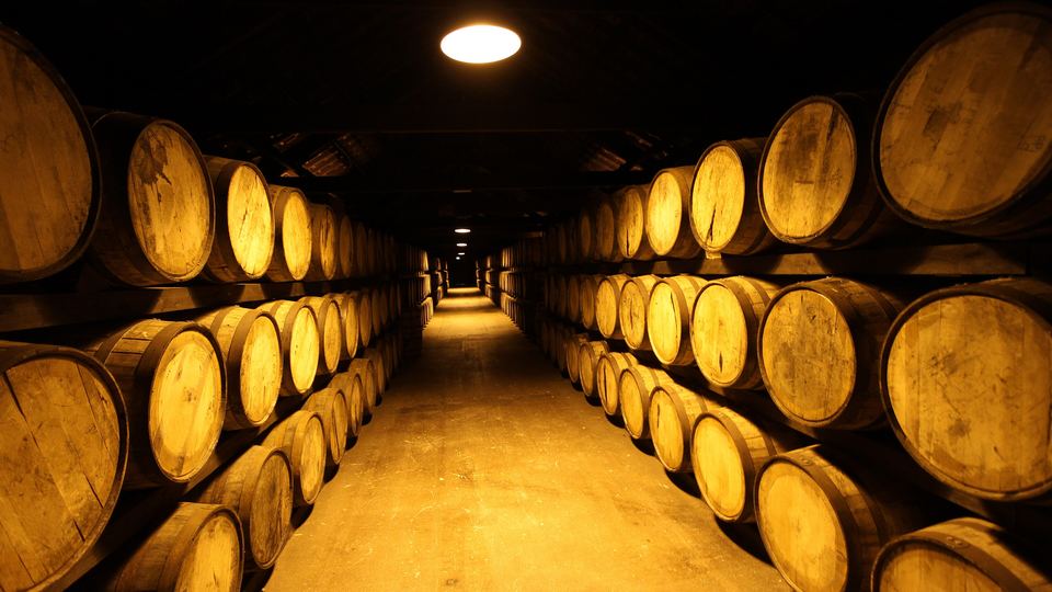 Long aisle of oak whiskey casks stacked in a dimly lit maturation warehouse at Midleton, Ireland